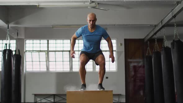 Fit caucasian man jumping on pylo box at the gym alt