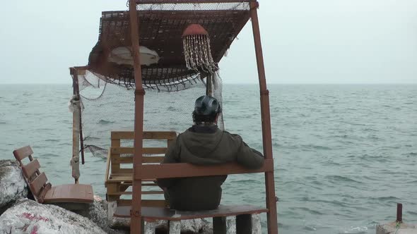 Lonely Man Sitting In Wooden Historical Fisherman Building And Looking Sea alt