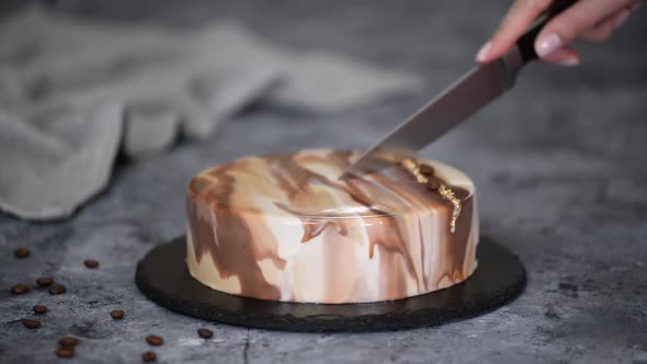 Female Hands Cut Coffee Mousse Cake Covered with Mirror Glaze