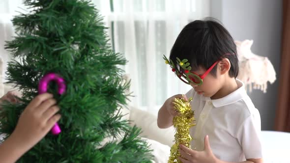 Asian Child Hanging Decorative Toy Together On Christmas Tree alt