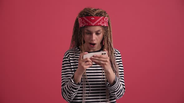 Cheerful hippie woman playing digital game on phone alt