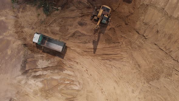 Aerial top view: yellow excavator pouring soil into tipper. alt