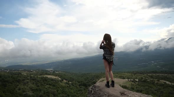 A Lonely Girl in Sporting Black Boots Stands on a High Hill in the Mountains