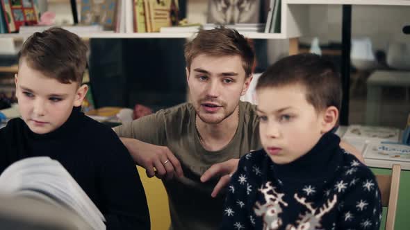 Attractive Young Male Teacher with Couple Tattooes on His Arms Explaining Something to Two Little alt