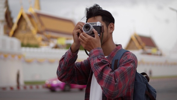 An attractive handsome tourist Asian man uses a film camera to take a photo of Wat Phra Kaew temple.