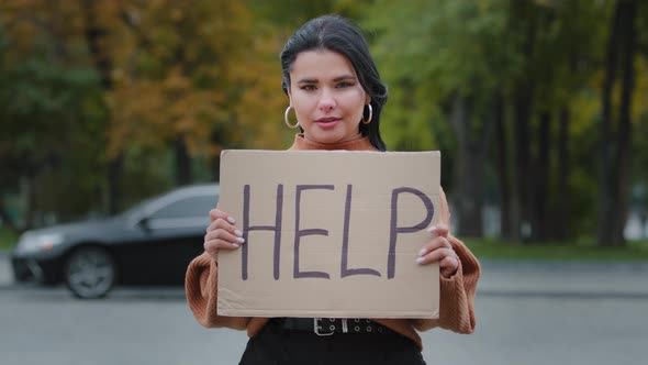 Closeup Sad Young Woman Stands Outdoors Near Roadway Holding Cardboard Sign with Words HELP Upset alt
