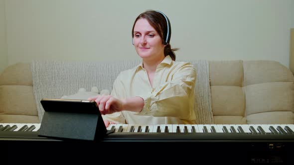 Woman musician with tablet playing electronic piano at home on sofa in living room