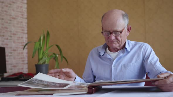 Old Elderly Lonely Man in Glasses for Sight Recalls Happy Moments of His Youth Leafing Through Photo alt