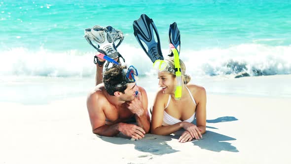 Couple wearing diving mask and flippers lying on beach alt