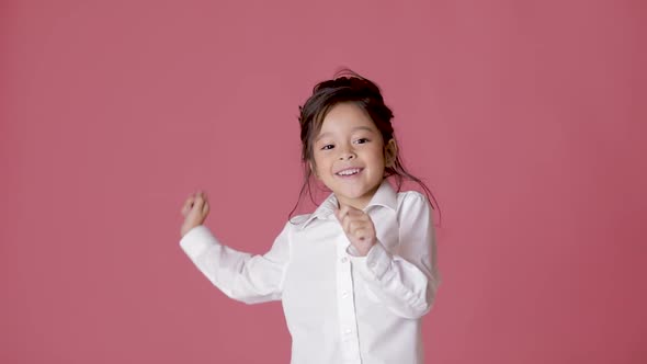 Little Child Girl in White Shirt Dancing on Pink Background