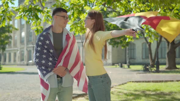 Portrait of Happy American Male Student Wrapped in National Flag Standing with Smiling Beautiful alt