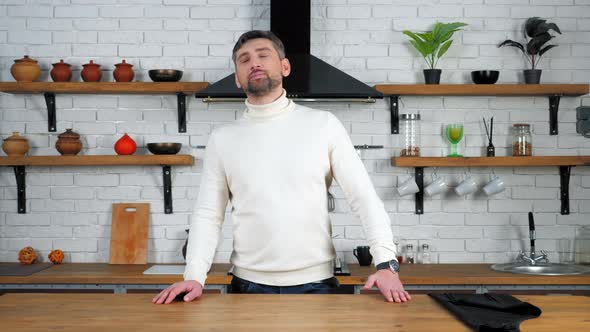 Pensive man stands in home kitchen near table looking up with open mouth alt