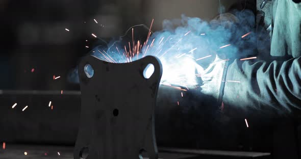 Worker Welding Metal Carefully At A Factory - Heat And Sparks From Welding Tool 