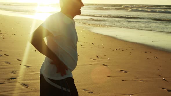 Senior man doing stretching exercise on beach alt