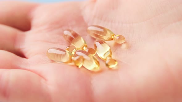Close up of hand holding yellow transparent capsules pills organic vitamins fish oil alt