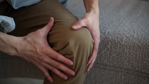 Man Massages Knee Feeling Acute Joint Pain Sitting on Sofa alt