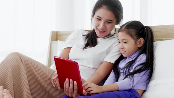 Happy mother with little girl are making selfie or video call to father or relatives in Bed