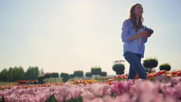 Happy Woman Touching Flowers at Walk with Camera in Tulip Field in Sunny Day alt