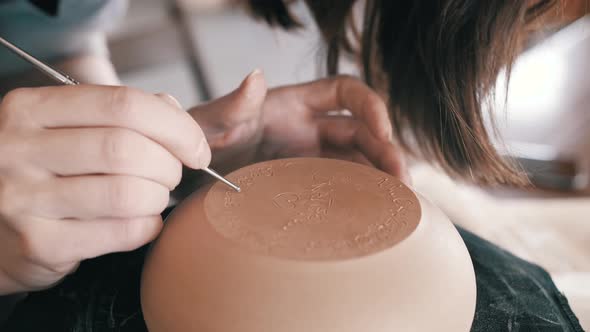The girl signs a vase of clay on a potter's wheel.