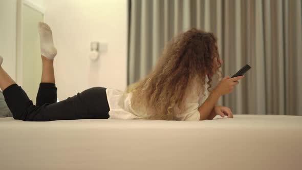 Mixed Race Young Woman Switches Television Channels on Bed alt