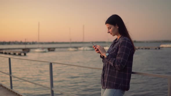 Attractive Woman Using Smartphone Chatting Outdoor on Sunset Near the Water