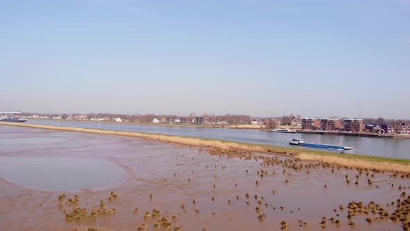Aerial Dolly Right Across Crezeepolder Nature Reserve Rising Above River Noord With Ship Passing By alt