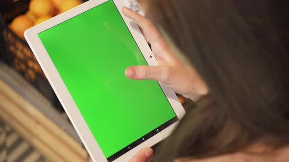 Closeup of a Young Woman's Hand Holding a Tablet Computer with a Green Screen Layout alt
