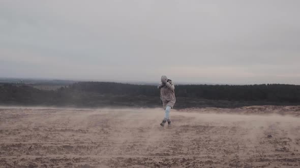 Wide Background Shot, Young Female Tourist Struggles To Walk Under Extreme Wind on Sand Dunes in alt