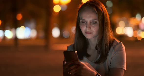 Young Girl in the Night City Writes Text Messages in a Smartphone alt
