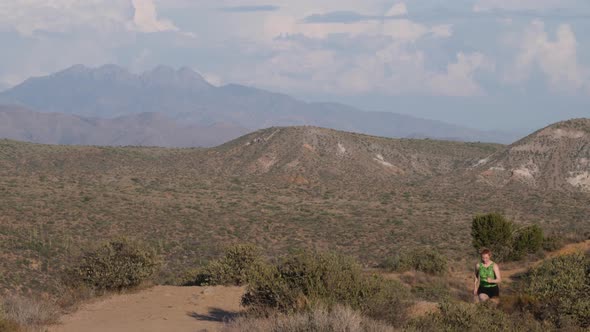 Short-haired woman runs on a trail in the Arizona desert. alt