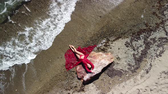 Top Aerial View on a Young Sensual Blonde Woman in Red Bikini Lying on the Rock Near Water at Sea alt