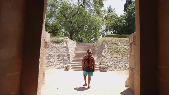 Backpacker Walking Towards A Stairway Outside A Temple Ruin In Hampi, India - forwarding shot alt