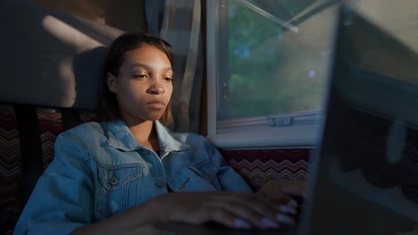 African Female Freelancer Working at a Laptop While Sitting in a Car Typing Text and Remote Work in alt