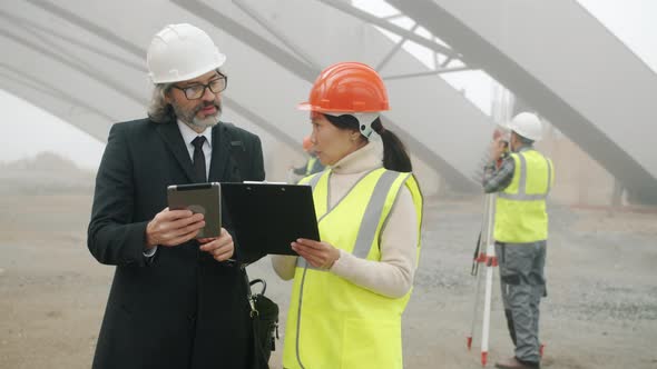 Asial Woman Engineer Talking to Caucasian Man Investor Discussing Construction Project Reading alt