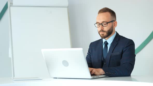 Attractive Businessman in Suit and Glasses Working with Laptop in White Office alt