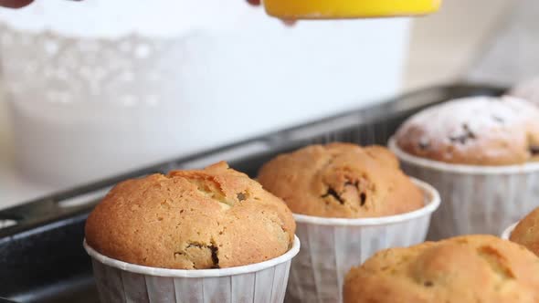 A Woman Sprinkles Icing Sugar On Freshly Baked Muffins. alt
