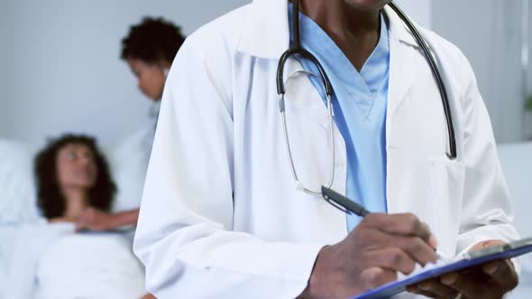 Close-up of African american doctor looking at camera while writing on clipboard in the ward 4k alt