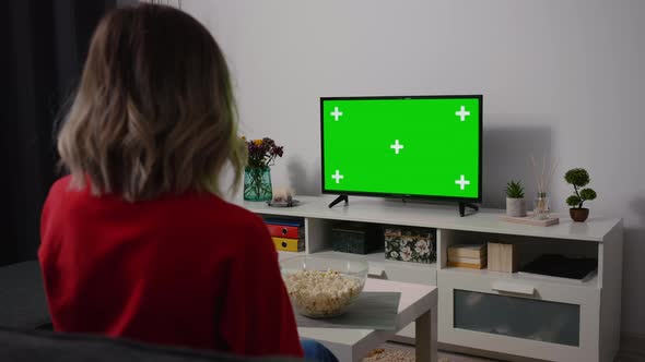 Woman watching TV focused eating popcorn. Green Screen TV Chroma Key. alt
