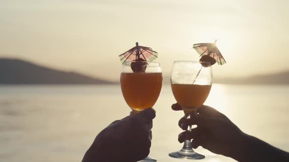Slow Motion Closeup of Knocking Glasses with Cocktails at Sunset alt