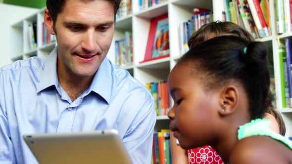 Teacher and schoolkids using digital tablet in library at school alt