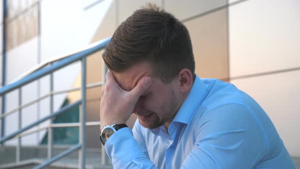 Side View of Upset Sad Businessman Sitting on Stairs Near Office Building and Crying. Desperate alt