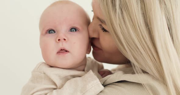 Closeup of a Young Mother Blonde Holding a Newborn Baby in Her Arms Indoors Kissing Him alt