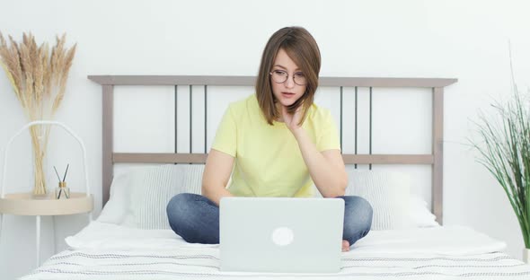 Young Beautiful Woman is Sittting on the Bed in Front of a Laptop