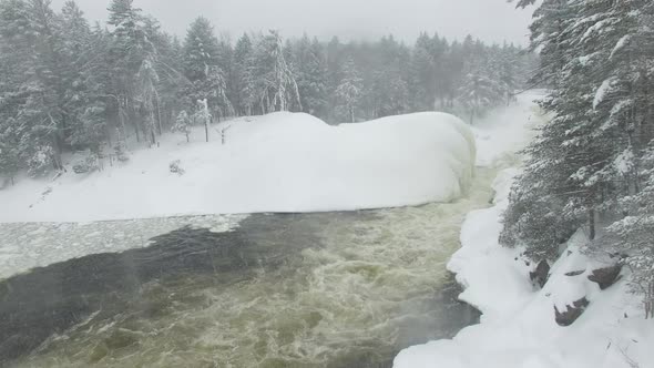 Slow rising drone filming forest's edge with snow covered pine trees and river alt