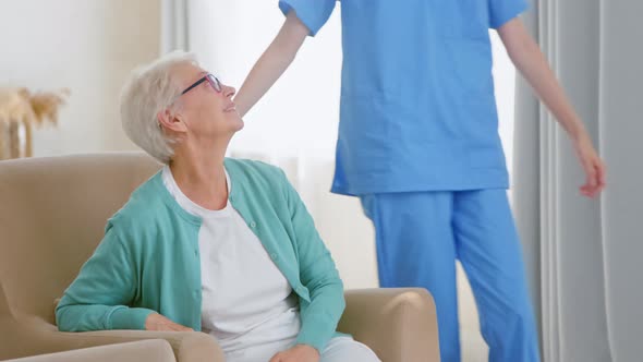 Positive nurse in blue uniform comes to hug lonely senior woman alt