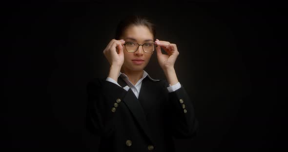 Beautiful Businesswoman Puts on Glasses on Black Background