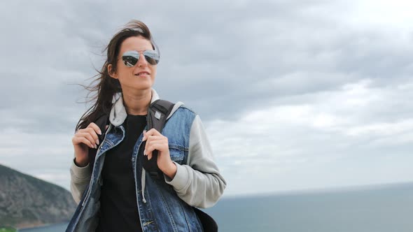 Woman in Sunglasses Standing on Mountain Top at Windy Overcast Weather Low Angle alt
