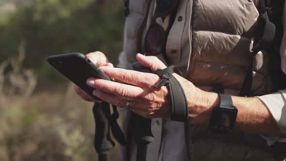 Close up view of senior woman holding smartphone in forest alt