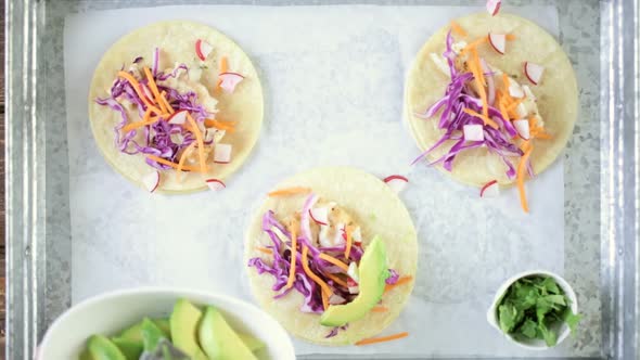 Preparing fresh fish tacos with cod and purple cabbage on a white corn tortillas. alt