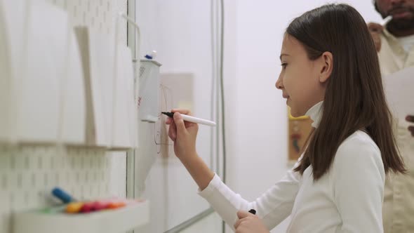 Girl Student Draws a Car on the Chalkboard While the African American Teacher Teaches Her alt
